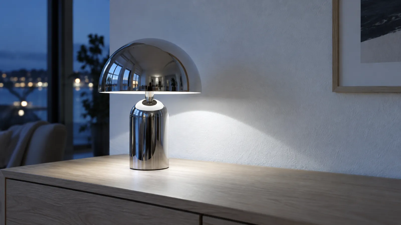 Bordslampa i blankpolerad krom på en ekbyrå, med skarp ljuspöl nedåt och en spegelblank reflex i metallen